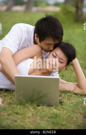 Young man kissing a young woman lying in front of a laptop Stock Photo