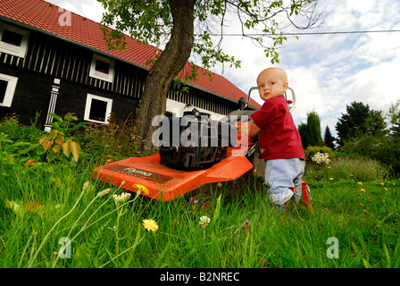 Young little one 1 year boy mowing the lawn Stock Photo