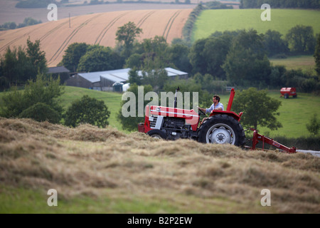 farmer sitting on a massey ferguson 185 old tractor pulling a haymaker attachment in a field making hay county down northern ireland Stock Photo