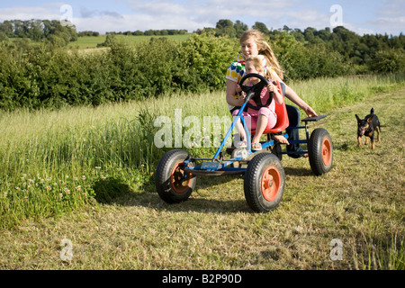 Children having fun on pedal go cart in farm field Cotswolds UK Stock Photo
