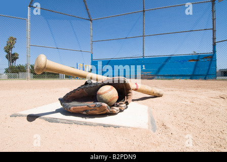 A baseball bat glove and ball lie on top of home plate as a conceptual sports image Stock Photo