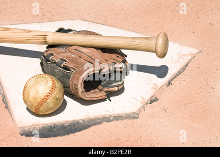 A baseball bat glove and ball lie on top of home plate as a conceptual sports image Stock Photo