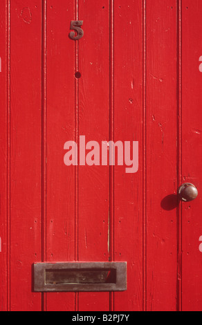 Solid wooden front door painted scarlet red with number 5 letterbox doorknob and peephole Stock Photo