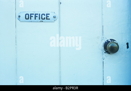 Solid wide-planked wooden door painted white with old-fashioned black and white sign stating Office with brass doorknob Stock Photo
