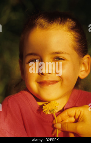 Young girl with dandelion put under her chin smiling summer game with mom 'Likes Butter' Bothell Washington State USA MR Stock Photo