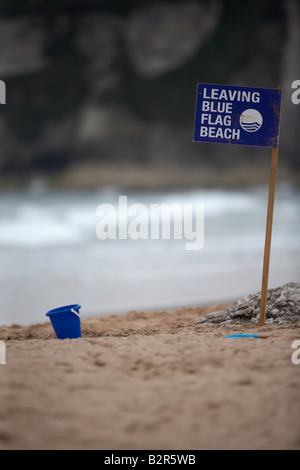 leaving blue flag beach sign with abandoned blue childs plastic bucket on white rocks beach county antrim northern ireland Stock Photo