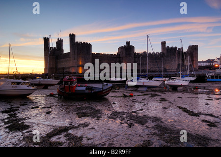 Caernarfon castle on the coast of North Wales illuminated at night with the boats in the estuary beached on the low tide Stock Photo
