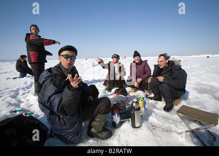 A group of Russians are ice fishing on the Sea of Okhotsk near Sakhalin island, Russian Federation. This usually involves snacks Stock Photo