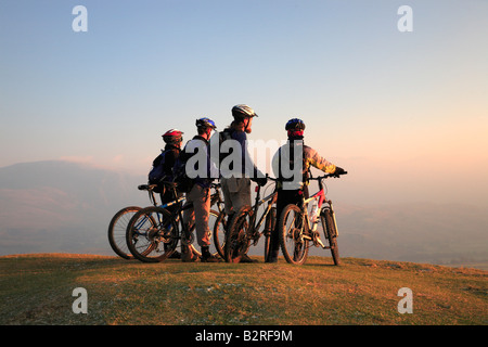 Group of mountain bikers take time to watch the sunset on top of a mountain. Stock Photo