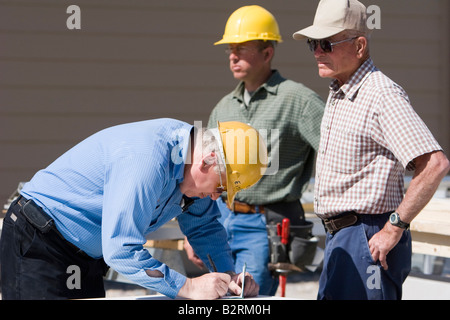 A construction foreman signs paperwork on a job site Stock Photo