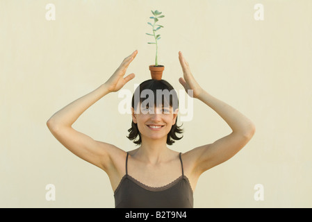 Woman balancing small potted plant on head, smiling at camera, portrait Stock Photo
