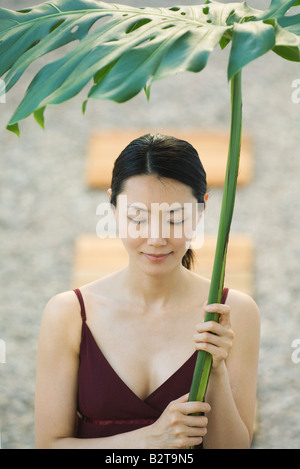 Woman holding palm leaf over her head, eyes closed, smiling Stock Photo