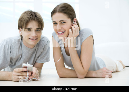 Young friends listening to MP3 player together, both lying on stomach on the floor Stock Photo