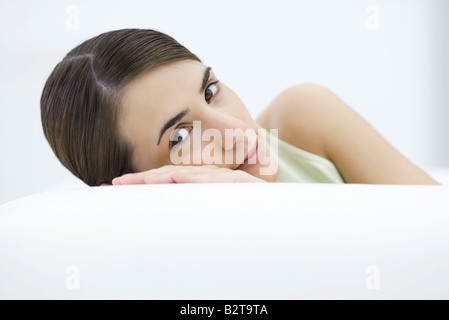 Woman leaning against side of sofa, head resting on hand, smiling at camera Stock Photo
