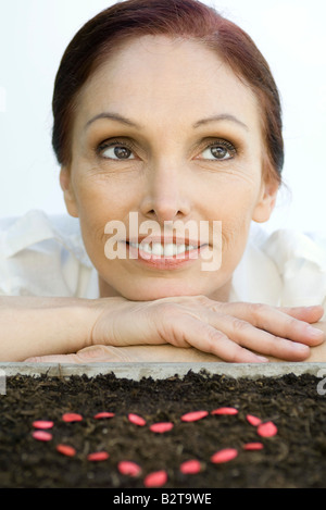 Mature woman with heart shape made of seeds on soil Stock Photo