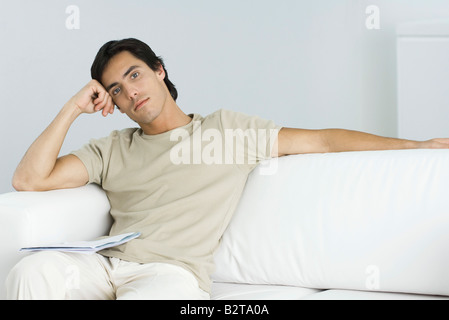 Man relaxing on sofa, looking at camera, leaning on elbow