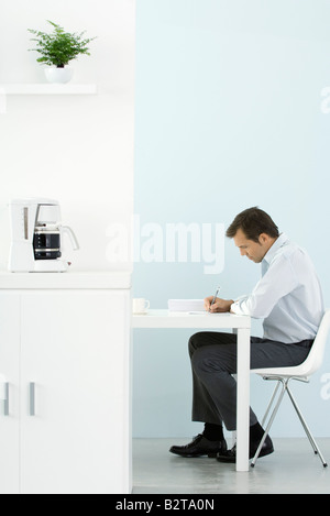 Man sitting at desk, working, coffee maker on counter in foreground Stock Photo