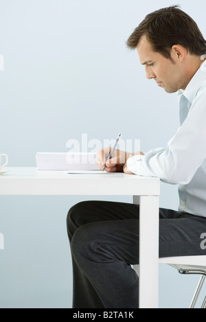 Man sitting at table, writing, side view Stock Photo