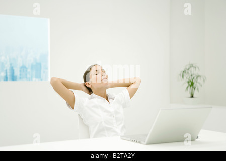 Woman leaning back at desk, hands behind head, eyes closed Stock Photo