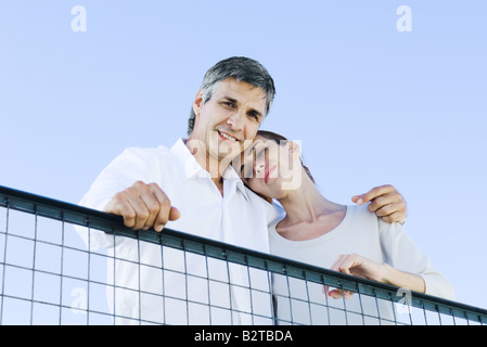 Couple looking down over wire fence at camera, low angle view Stock Photo