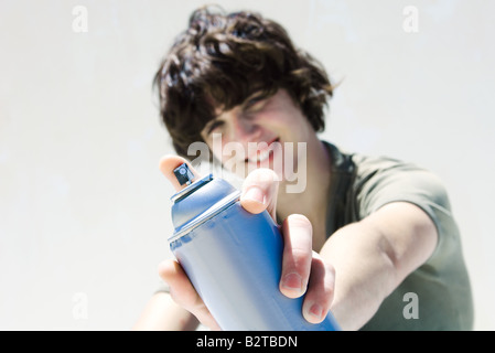 Teenage boy pointing can of spray paint at camera, focus on the foreground