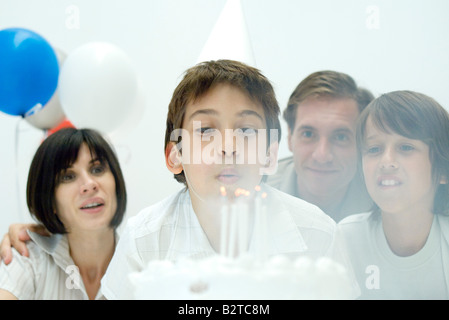 Boy blowing out candles on birthday cake, family watching Stock Photo