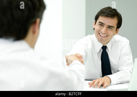 Two businessmen shaking hands, over the shoulder view Stock Photo