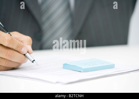 Man with adhesive note and document, holding pen, cropped view Stock Photo
