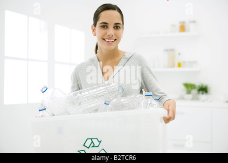 Teen girl carrying recycling bin full of plastic bottles, smiling at camera Stock Photo