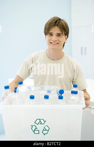 Young man carrying recycling bin filled with plastic bottles, smiling at camera Stock Photo