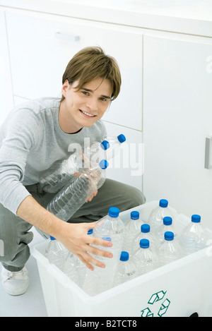 Young man putting plastic bottles in recycling bin, smiling at camera Stock Photo