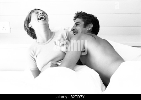 Couple in bed, both laughing Stock Photo