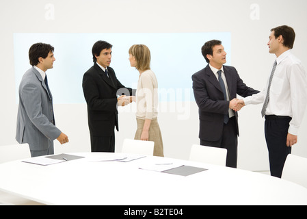 Group of professionals standing beside table, smiling, some shaking hands Stock Photo