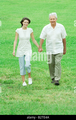 Grandfather and teen granddaughter walking outdoors, holding hands, smiling at camera Stock Photo