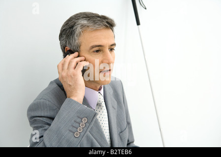 Businessman using cell phone, white cane leaning beside him Stock Photo