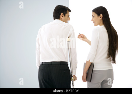 Colleagues standing side by side, chatting, one using crutches Stock Photo
