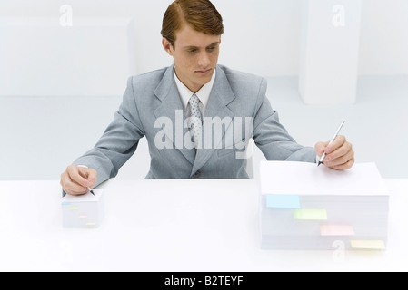 Businessman writing on two stacks of paper, one large, one small, pencil in each hand Stock Photo