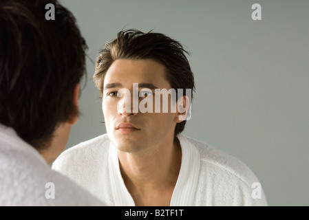 Man examining his face in the mirror, wearing bathrobe Stock Photo