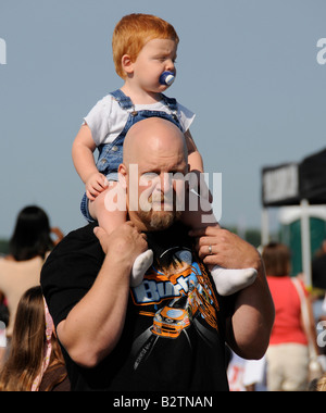 Young boy  sitting on fathers shoulder at airshow. Stock Photo