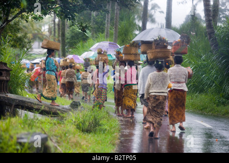 Procession of Hindu women and children carrying offerings in baskets to bless the harvest during a tropical rain storm Stock Photo