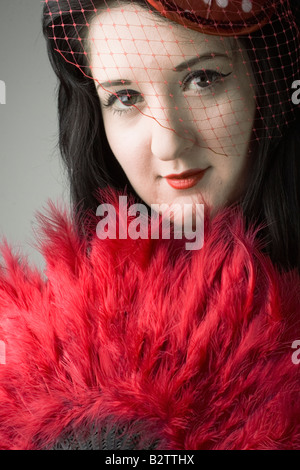 Burlesque portrait of a young brunette woman holding a red feather fan.