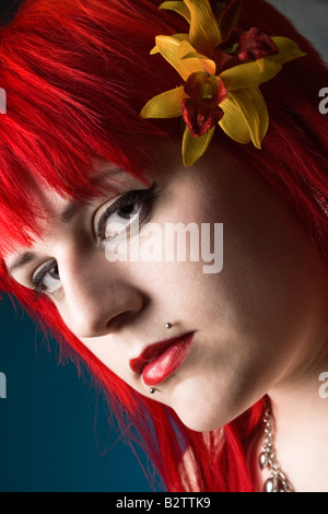 Headshot portrait of a young goth girl with bright red hairr on a blue background. Stock Photo