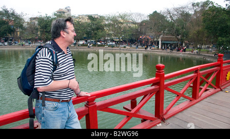 Tourist stands on the well known red Morning Sunlight or Huc Bridge at Hoan Kiem Lake Hanoi Vietnam Stock Photo