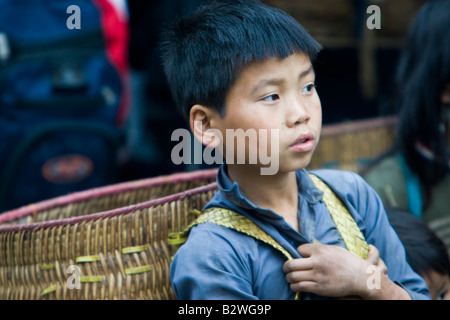 Black Hmong hilltribe boy with traditional shoulder basket waits at market Sapa Vietnam Stock Photo