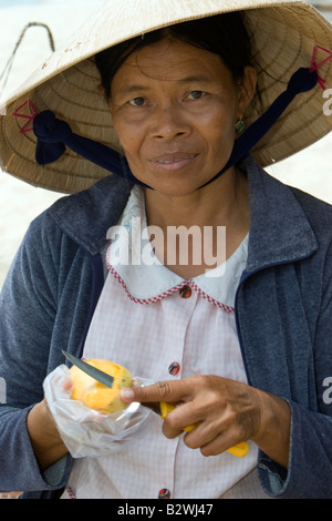 Conical hat woman tropical  fruit vendor prepares mango slice snack Long Beach Phu Quoc Island Vietnam Stock Photo