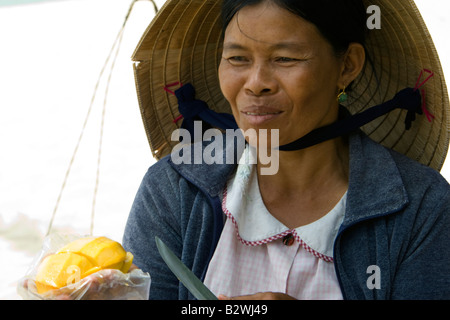 Conical hat woman tropical  fruit vendor prepares mango slice snack Long Beach Phu Quoc Island Vietnam Stock Photo