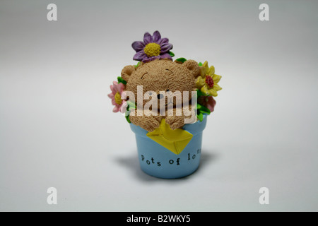 Cute smiling teddy bear in a blue pot of beautiful flowers holding a message of love and peace to be delivered to his valentine Stock Photo