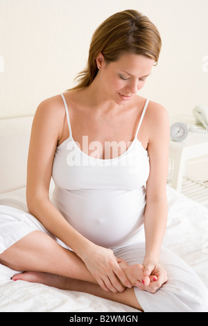 Pregnant woman sitting in bed rubbing feet Stock Photo