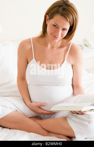 Pregnant woman in bedroom reading book smiling Stock Photo