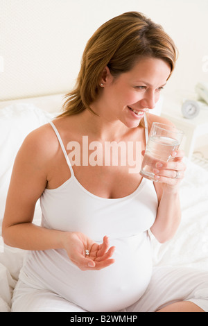 Pregnant woman in bedroom holding medicine and water smiling Stock Photo